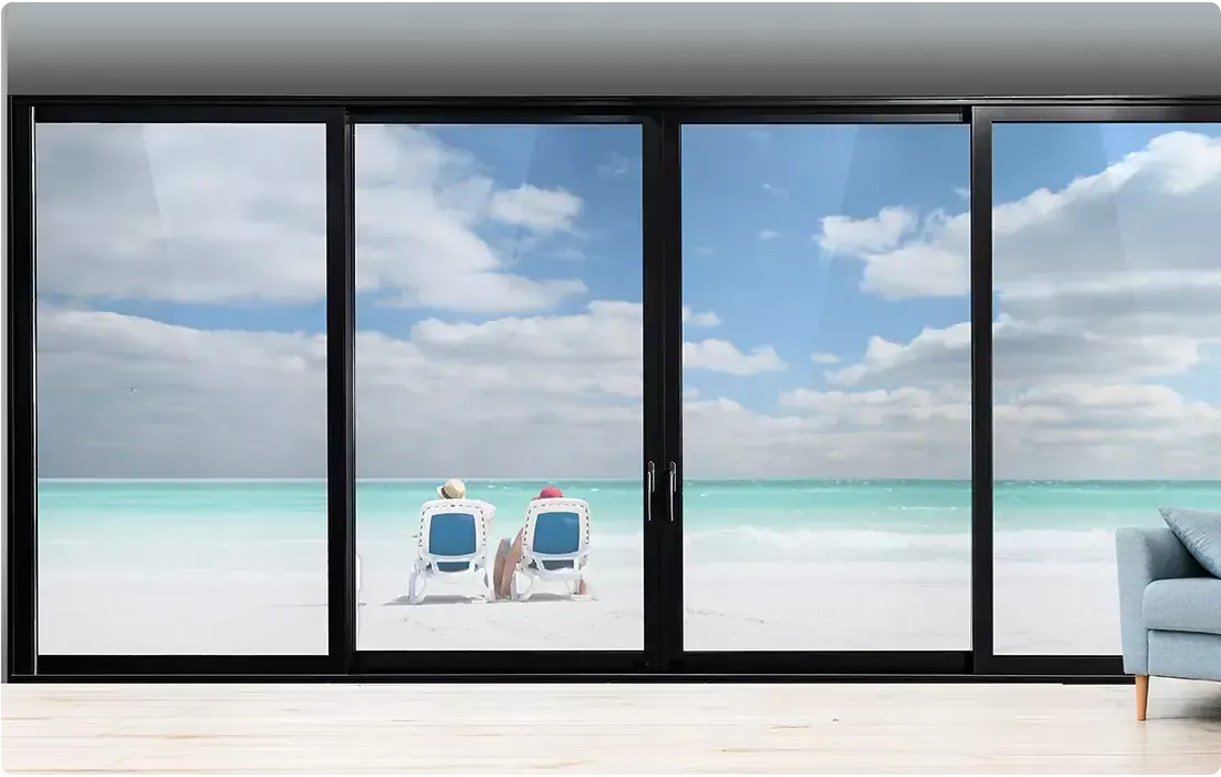 Two people relax on a white sand beach viewed through sliding glass doors.