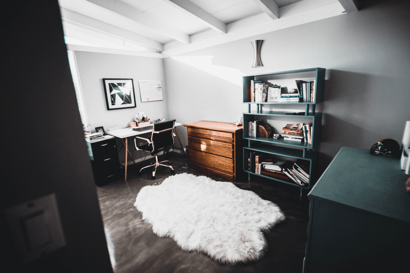 A modern home office with a desk, office chair, bookshelf, and fluffy white rug.