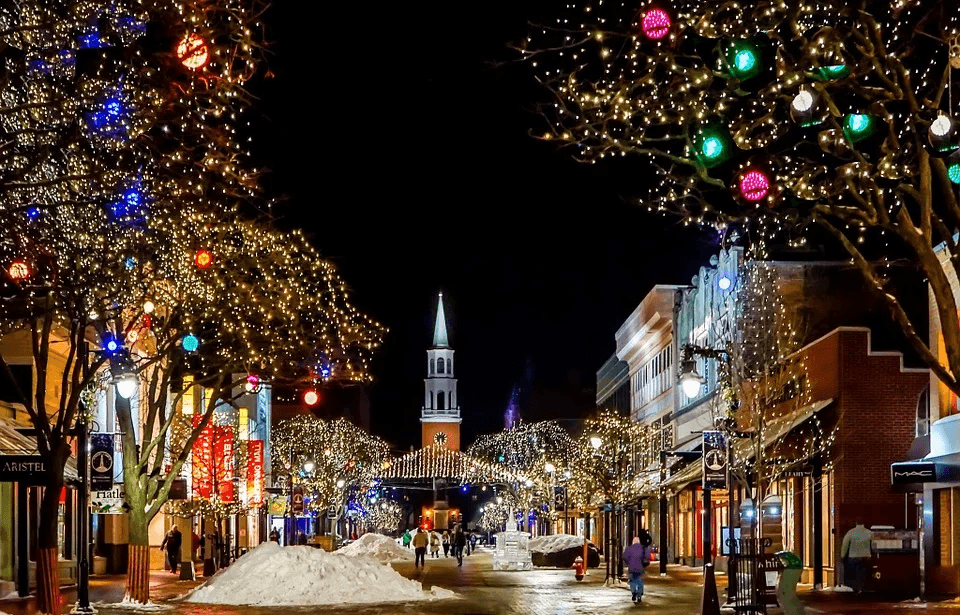 Nighttime street with festive Christmas lights, snow, and a prominent church steeple.