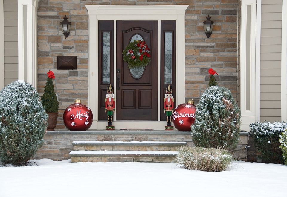 Snow-dusted front door decorated for Christmas with wreath, nutcrackers, and large red ornaments.