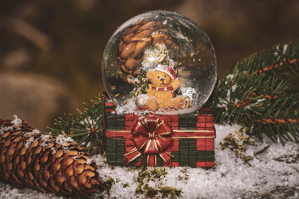 Snow globe with a teddy bear in a Santa hat, surrounded by pine cones and snow.