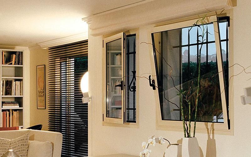Open wooden-framed windows with security bars provide light in a cozy living room.