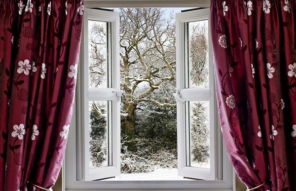 Open window with red floral curtains revealing a snowy winter landscape and bare trees.