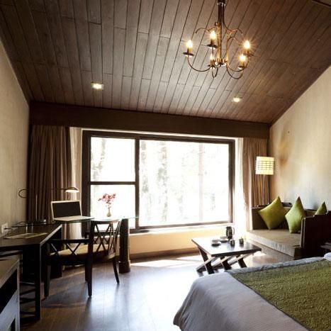 A spacious hotel room with a large window, wooden ceiling, and cozy seating area.