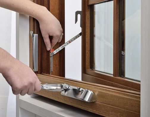 Hands measuring a wooden casement window frame with a measuring tape and crank.
