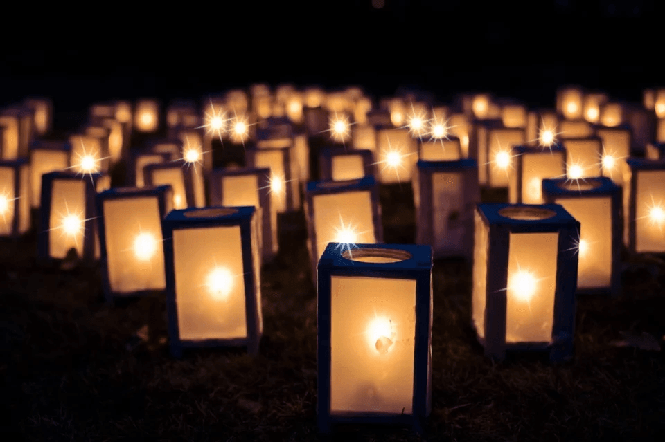 Many glowing white paper lanterns illuminate dark ground at night, creating a peaceful atmosphere.