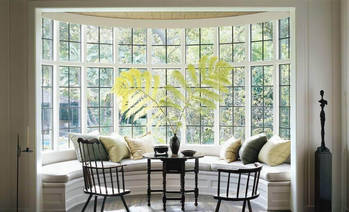 Large bay window with built-in seat, cushions, two black chairs, and greenery outside.