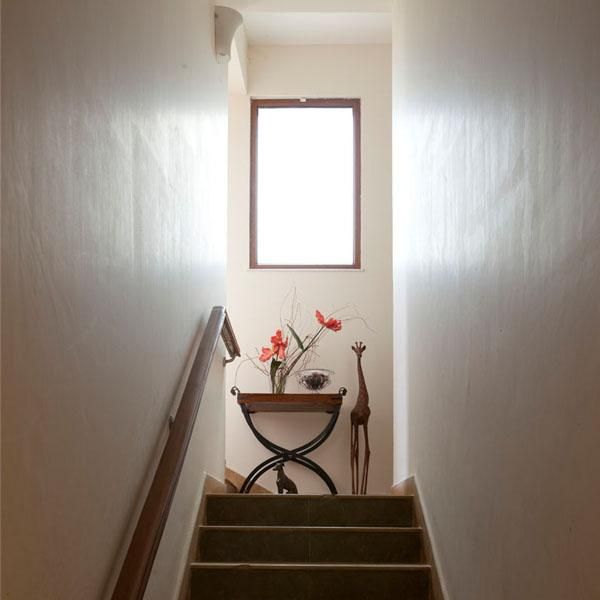 Staircase ascends to a landing with flowers on a table beneath a bright window.