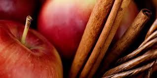 Red apples and cinnamon sticks nestled together in a rustic woven basket.