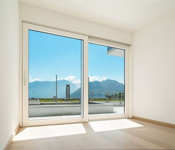 Empty room with white walls and large sliding glass door revealing mountains under blue sky.
