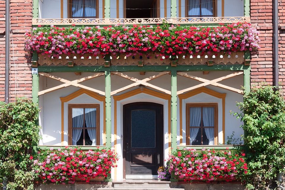 Traditional building facade with vibrant red and pink flowers in window boxes and decorative beams.