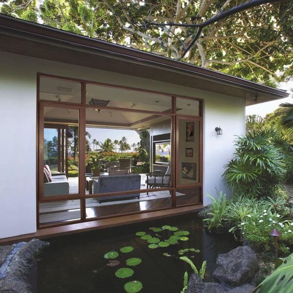 Modern house with large glass windows overlooks a peaceful pond with lily pads.