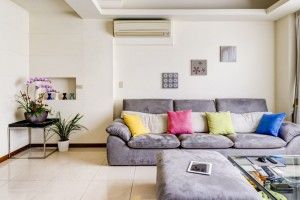 A modern living room features a gray sofa, colorful pillows, and an ottoman.