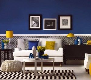 Modern living room featuring royal blue walls, white sofa, yellow accents, and a striped rug.