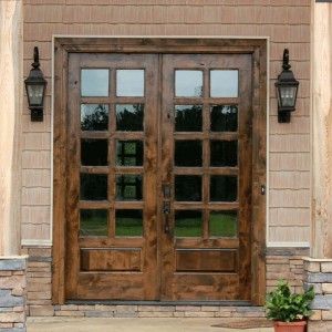 Rustic wooden double doors with multiple glass panes, flanked by black lantern sconces.
