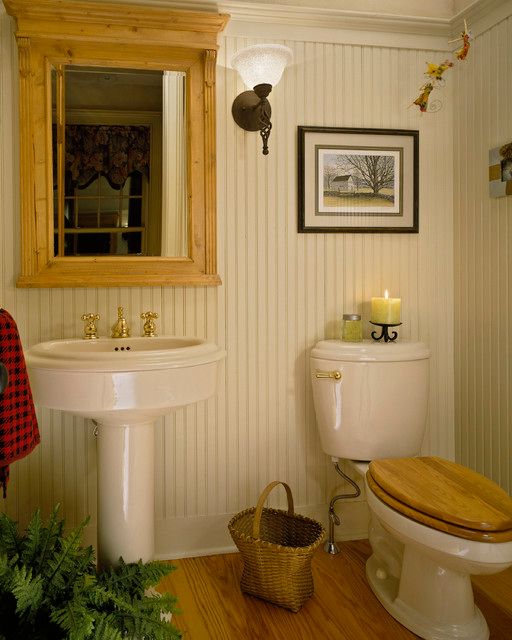 Rustic bathroom with a wooden mirror, pedestal sink, and toilet with a wooden seat.