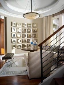 Sophisticated entryway with a curved gallery wall of framed photos, a table, and staircase.