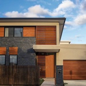 Modern house exterior featuring beige walls, dark stone, and warm wooden shutters under a blue sky.