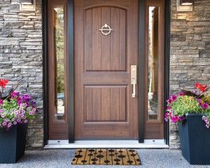 Brown wooden front door with side windows, stone facade, and colorful flower pots.