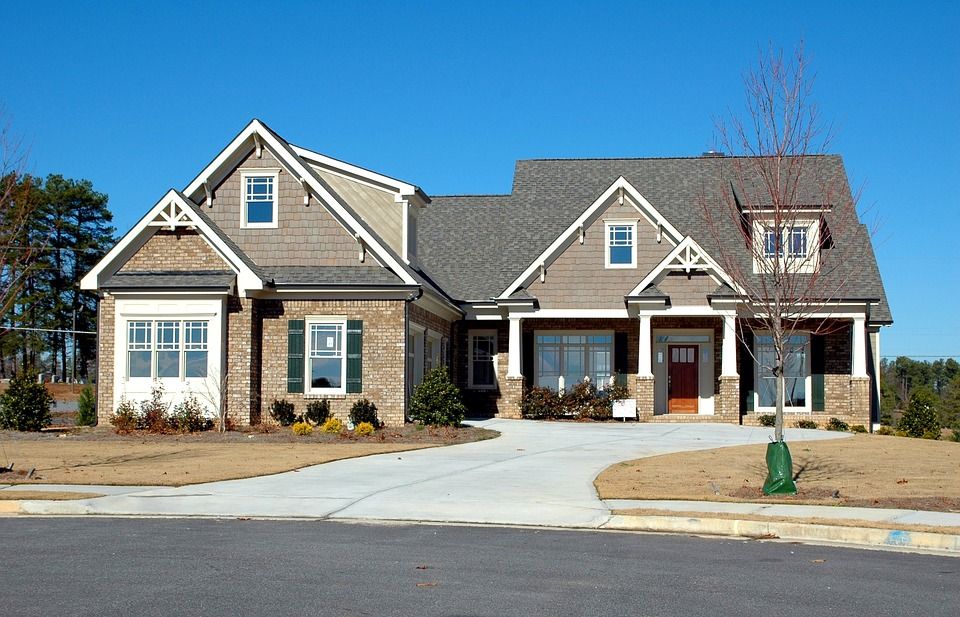 Modern suburban house with a gray roof, brick and siding, and a wide paved driveway.