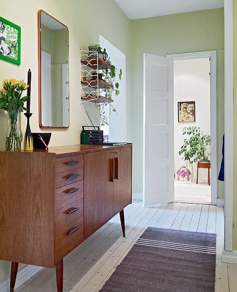 Mid-century modern credenza with mirror and flowers in a light green hallway with a rug.