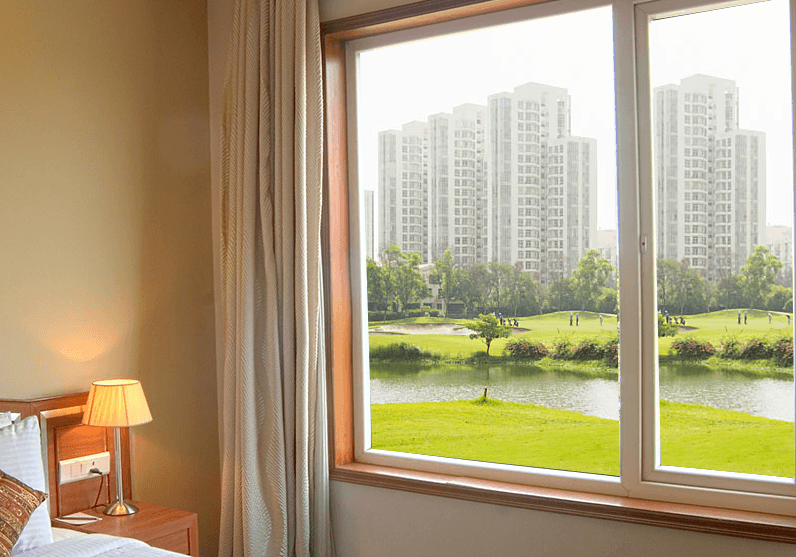 View from a modern room window showing a park, lake, and distant apartment buildings.