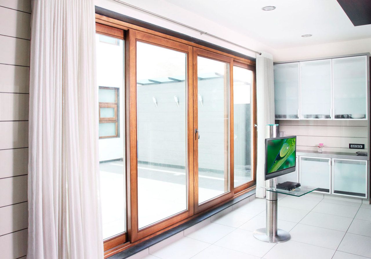 Modern room featuring large wooden-framed sliding glass doors and a sleek white kitchen area.