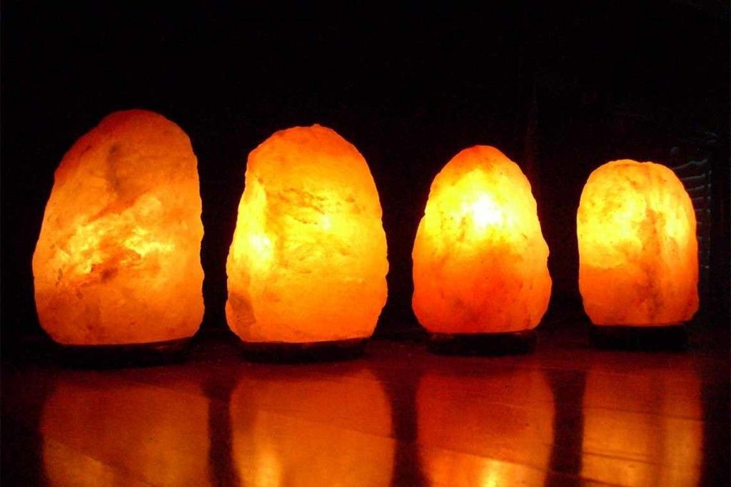 Four glowing Himalayan salt lamps of different sizes emit a warm orange light in a dark room.