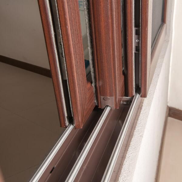 Close-up of a brown sliding window or door frame with its multi-track mechanism visible.