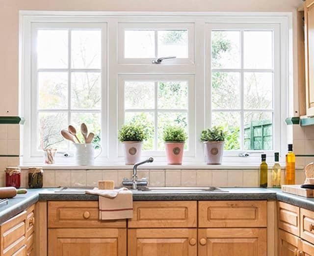 Bright kitchen sink area with a large window, potted plants, and light wood cabinets.