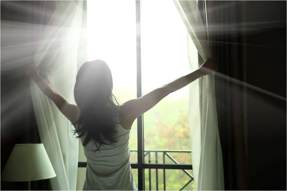 Person opening curtains, letting bright morning sunlight stream into a room.