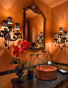 Luxurious bathroom with ornate gold mirror, black sconces, unique round sink, and red orchid.