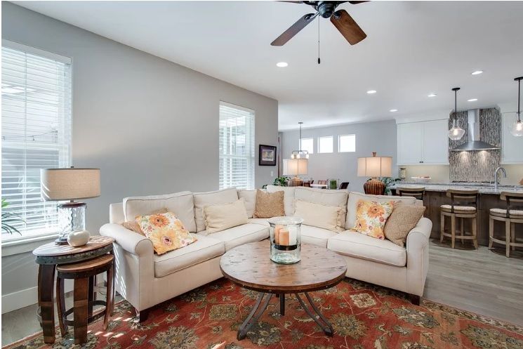 A bright living room with a cream L-shaped sofa, round wooden coffee table, and patterned rug.