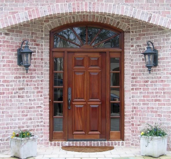Elegant wooden front door with sidelights, arched transom, and two lanterns on a brick house.