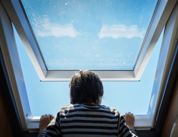 Person from behind looking up through a skylight at a clear blue sky.