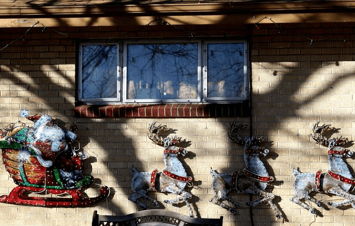 Lighted Santa in sleigh and reindeer Christmas decorations on a brick wall under a window.