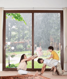 Family plays joyfully indoors by a large window overlooking a rainy garden.