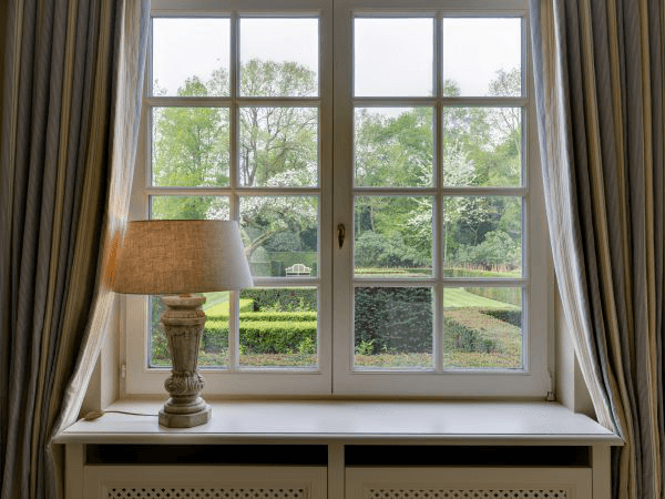 Elegant window with a lamp on the sill overlooking a vibrant green garden.