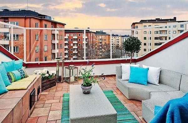 Chic rooftop terrace with grey furniture, blue cushions, and a city view at sunset.