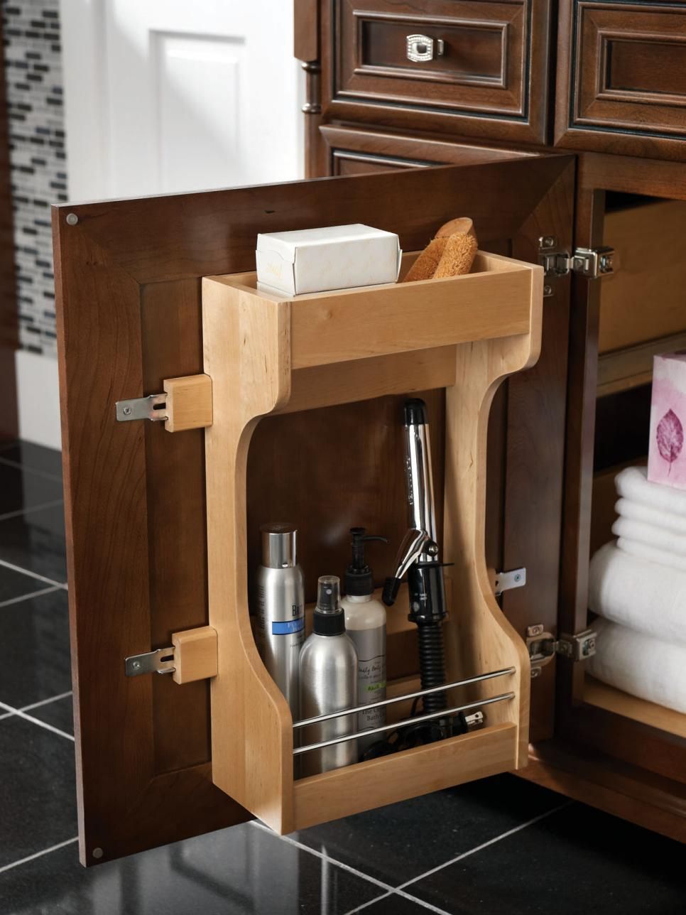 Wooden pull-out organizer holds toiletries inside a dark bathroom cabinet door.
