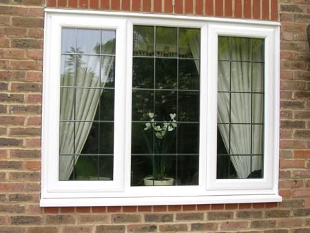 White framed bay window with gridded panes in a red brick wall, potted plant inside.