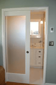 White pocket door with frosted glass panel partially open, revealing a bright bathroom vanity.
