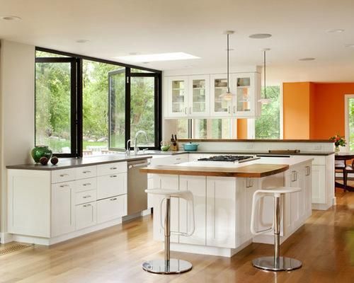 Modern kitchen with white cabinets, large island, and expansive windows overlooking greenery.