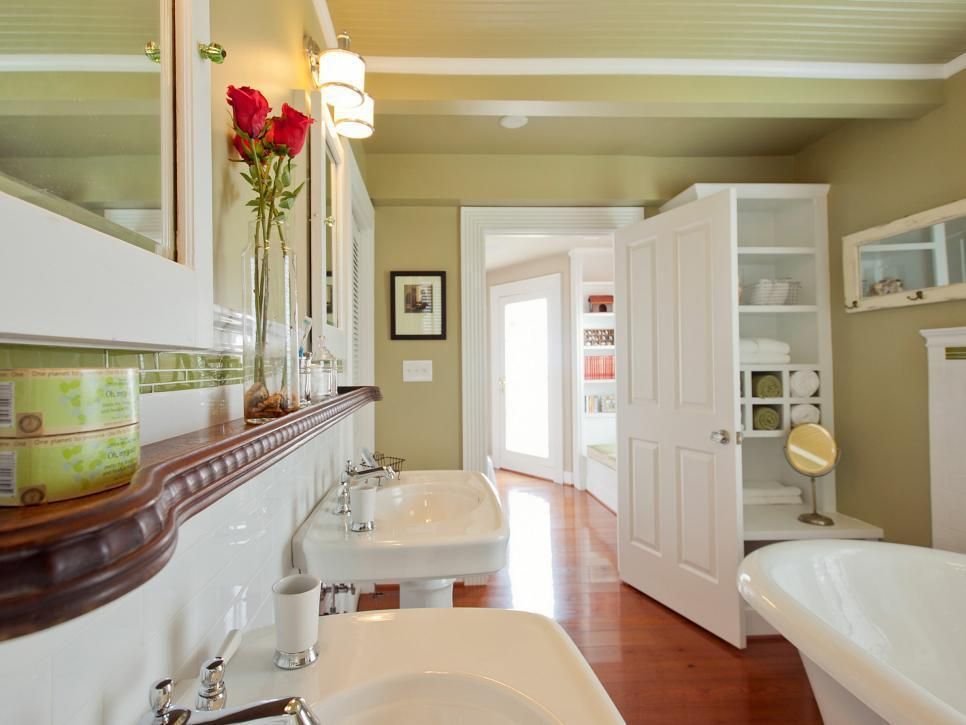 A bright bathroom features twin pedestal sinks, red roses, and a white clawfoot tub.