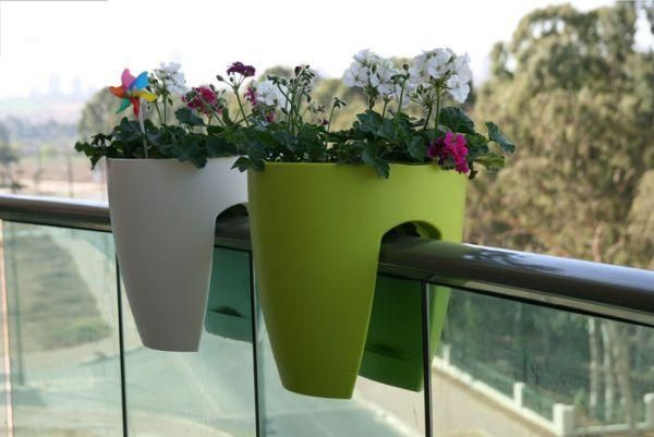Two balcony railing planters, white and green, filled with colorful geraniums.