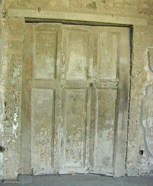 Weathered gray wooden door with panels set in an old, distressed building wall.