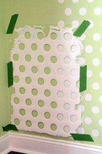 Rectangular stencil with circular cutouts taped to a green polka-dotted wall.