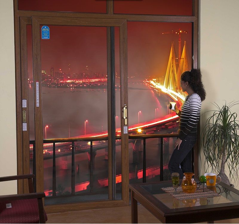 Woman by window observes a brightly lit bridge and city skyline at night.