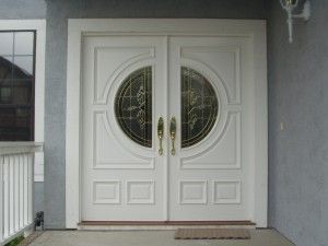 White double entry doors feature ornate circular glass inserts and polished gold handles.