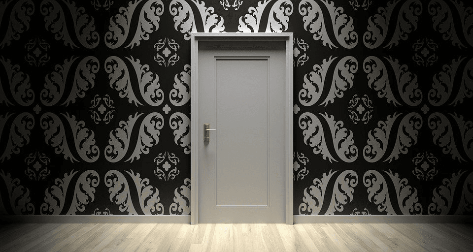Closed grey door in a room with black and silver damask patterned wallpaper.